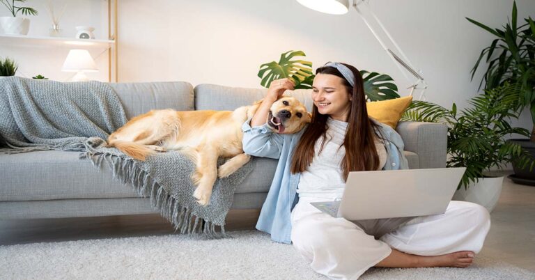 Happy woman sitting on the floor with her Golden Retriever lounging on a couch in a peaceful, cozy living room filled with greenery and natural light, illustrating tips on How to Create a Stress-Free Environment for Your Pet at Home.