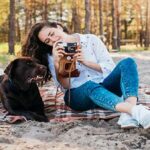 Young woman sitting on a blanket at a sandy beach with her dog, enjoying a day at one of the top pet-friendly vacation spots.