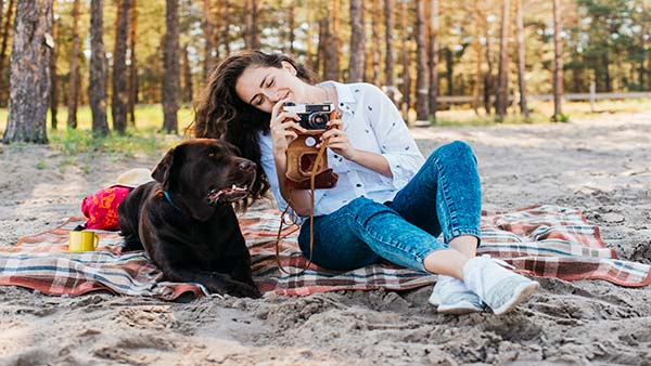 Young woman sitting on a blanket at a sandy beach with her dog, enjoying a day at one of the top pet-friendly vacation spots.