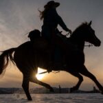 The silhouette of a cowgirl riding a horse against a sunset in an oceanic landscape, symbolizing freedom and strength. Perfect for inspiring quotes about horses and the bond between rider and steed.