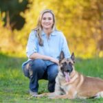 Alicia Collins posing with a German shepherd on a grassy ground. 